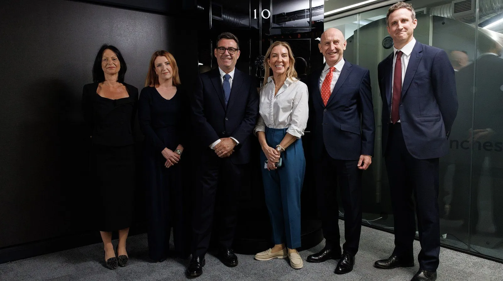 Prime Minister Andy Burnham and Chancellor John Healey standing with colleagues in front of a black Number 10 front door inside the government's No10 North office in Manchester